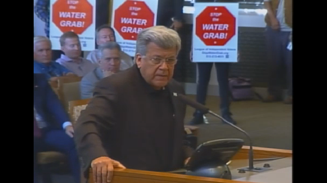 In this City Council meeting screenshot, San Antonio Water System Board of Trustees Chairman Heriberto "Berto" Guerra Jr. speaks to City Council October 30, urging approval of the Vista Ridge Pipeline while protestors stand behind him.