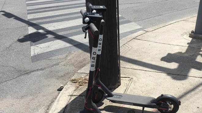 A pair of dockless scooters sit on a sidewalk along North St. Mary's Street.