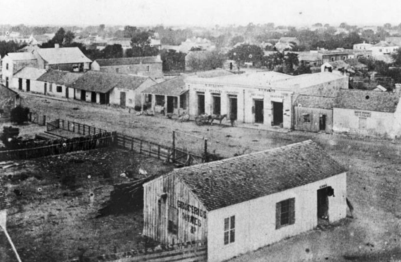 This view from the roof of the Menger Hotel shows a grocery store in the foreground. The store was located on the south end of Alamo Plaza in this 1866 photo. Yes, 1866!