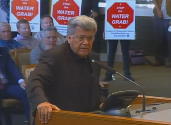 In this City Council meeting screenshot, San Antonio Water System Board of Trustees Chairman Heriberto "Berto" Guerra Jr. speaks to City Council October 30, urging approval of the Vista Ridge Pipeline while protestors stand behind him. - CURRENT