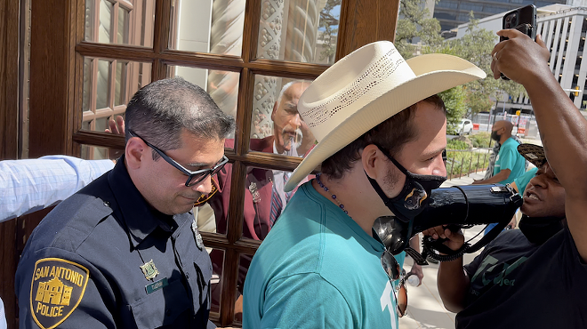 Ashton Condel, a housing justice organizer, is escorted out of City Hall by SAPD after demanding a meeting with Mayor Ron Nirenberg to discuss "dangerous" living conditions at the Seven Oaks Apartments.