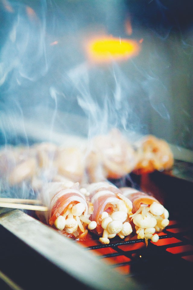 Bacon-wrapped enoki cooking on Izakaya Nin’s robata grill. - JOSH HUSKIN