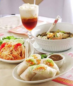 Clockwise from front: Thai summer rolls with special dipping sauce, green papaya salad, Thai iced tea, and a bowl of Jasmin noodle soup.