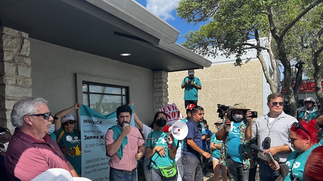 Congressional candidate Greg Casar (speaking into megaphone) addresses protesters Monday outside the offices of Achievement Investment Group.