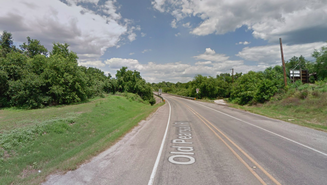 Fang Baby of Old Pearsall Road
In a tale that supposedly originated in the 1960s, a group of young guys were driving down Old Pearsall Road after a night of drinking when they had a creepy encounter. The driver saw something in the road that looked like a toddler, which appeared to be hurt, with blood around its mouth. He swerved to avoid the maybe-baby, but didn’t stop. The friends argued about what it was, and the driver ultimately decided that they should just go home. However, once home, he felt guilty that he had possibly left a baby in the middle of nowhere. Armed with a cooler of beer, he went back to Old Pearsall Road. Unfortunately, he got a flat, and found two small puncture marks in the tire. After replacing the tire, he cracked a beer and chilled in his car for a while before falling asleep. A sharp pain in his neck woke him up, where he found the fanged baby in his lap with a bloody mouth and shirt.
Photo via Google Maps