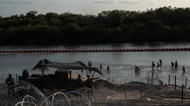 Migrants walk along the Rio Grande past recently installed buoys in Eagle Pass, Texas on July 29, 2023.