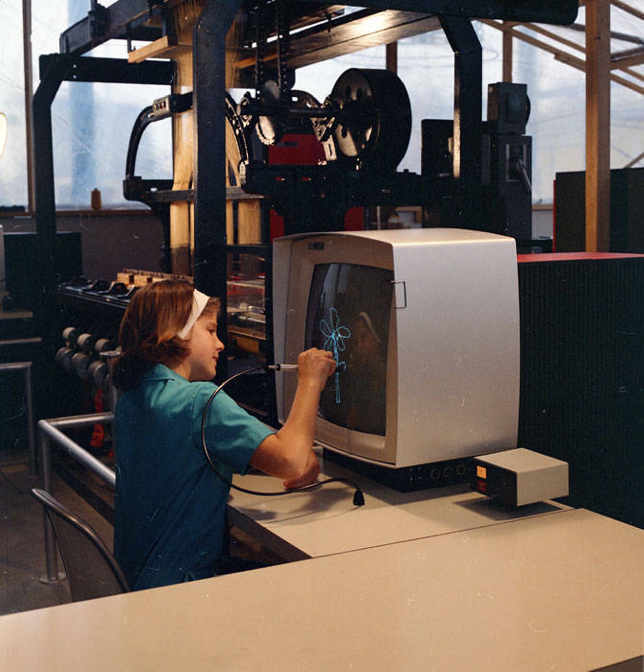 Girl uses a "light pen" to draw a design that a computer instructs a Jacquard loom to replicate in a four-inch swatch of woven fabric in the IBM Durango Pavilion