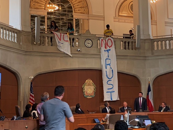Protestors lower banners during a city council meeting protesting this summer's delay of the paid sick time ordinance. - TWITTER / @MOVE_TEXAS