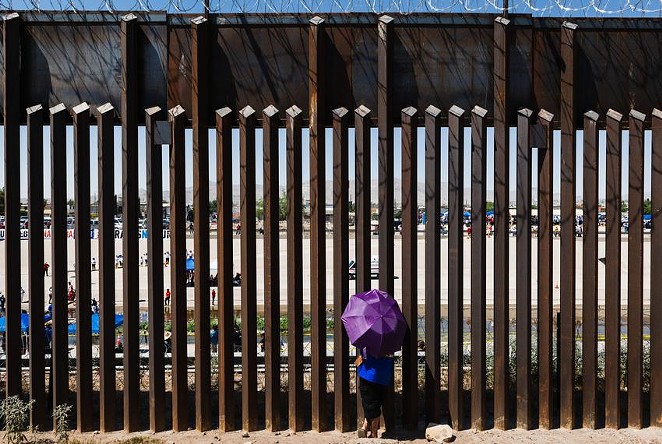 A woman looks through the border wall towards her family in Ciudad Juarez, Mexico from El Paso, Texas on June 19, 2021. - Justin Hamel / The Texas Tribune