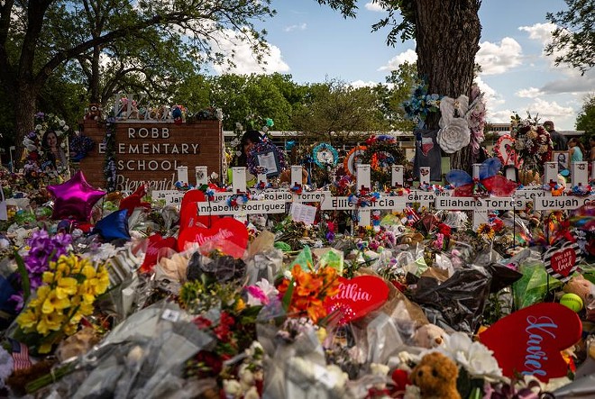 Flowers and gifts sit in front of wooden crosses memorializing the 21 victims of the May 24 mass shooting at Robb Elementary in Uvalde. - Texas Tribune / Kaylee Greenlee Beal