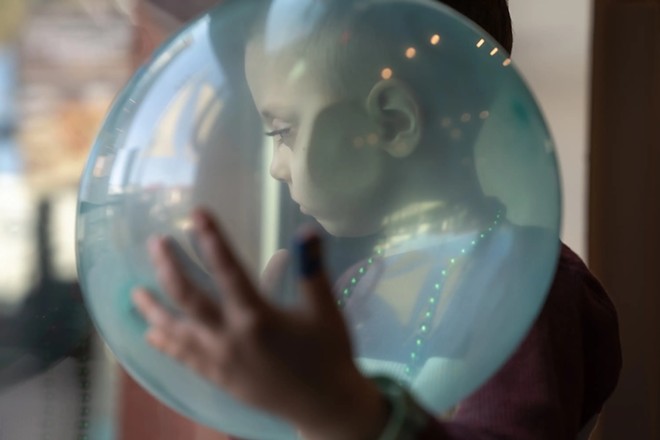 August Johansen looks through the glass door of the birthday venue while cradling a balloon on Dec. 9, 2023. He had inoperable brain cancer and depended on Medicaid to pay for full-time home nursing care from a private agency to help his mother take care of him throughout years of health crises. Last December, he became one of 810,000 children dropped from Texas’ Medicaid program in the previous five months, but was reinstated through his mother's efforts. - Texas Tribune / Azul Sordo