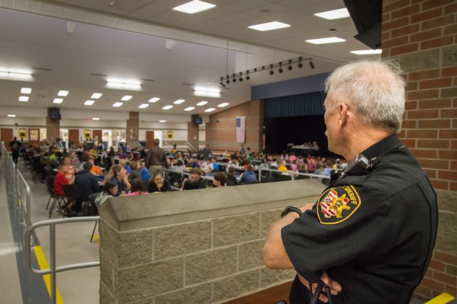 A security guard at an Ohio school looks out over students in the cafeteria at lunch time. - Shutterstock