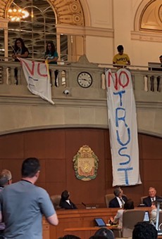 Protestors lower banners during a city council meeting protesting this summer's delay of the paid sick time ordinance.
