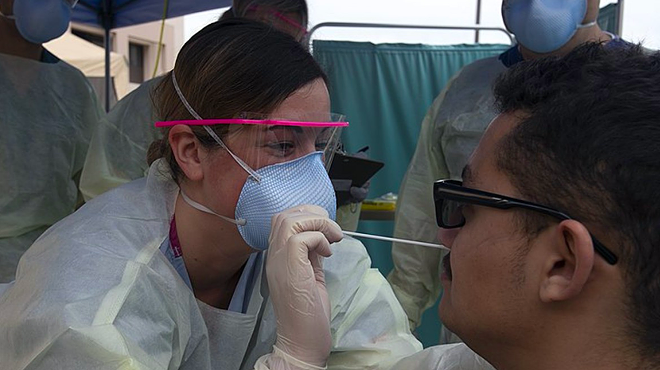 A medical technician swabs a patient at a COVID-19 testing site.